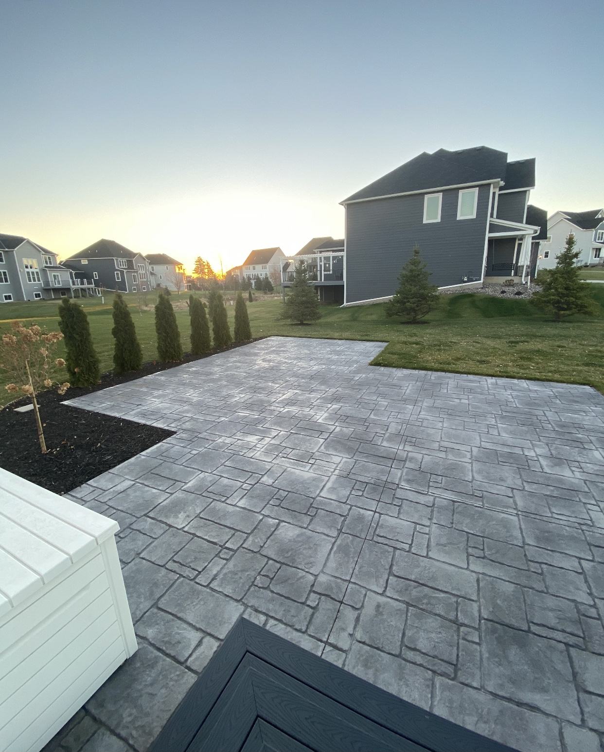 Ashlar pattern stamped concrete patio poured across a back yard at sunset, neighboring houses behind it